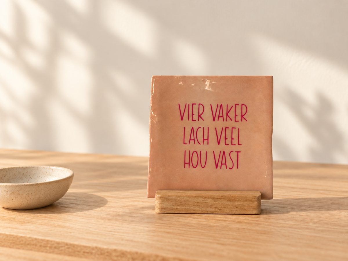 Roze tegeltje 'vier vaker, lach veel, hou vast' op een houten houder
